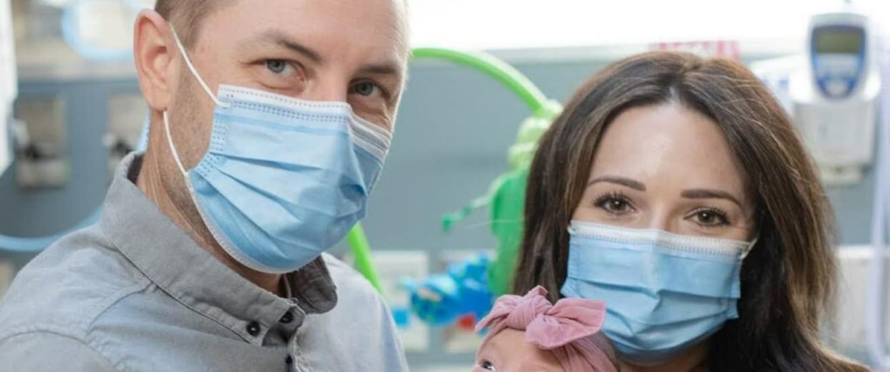 New parents with masks on holding newborn in the NICU