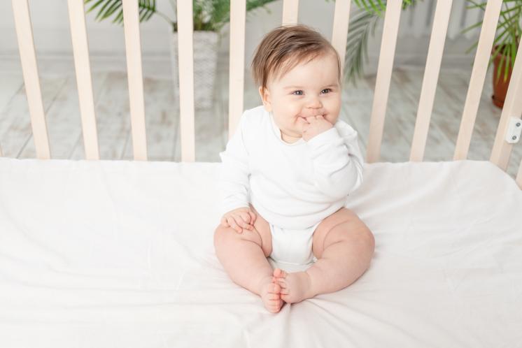baby that just learned to sit up sitting in a crib with mattress at the lowest setting
