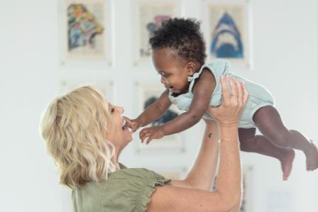 woman smiling holding baby up in front of her while baby smiles and reaches for her face
