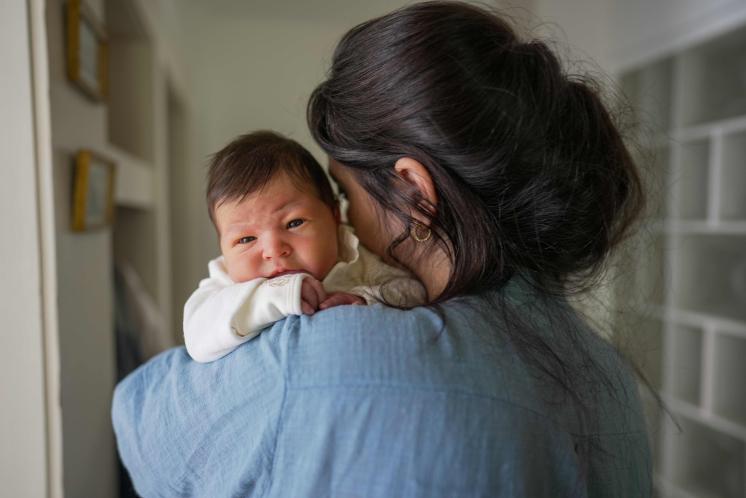 baby facing away from camera holding newborn over her shoulder who is wide awake