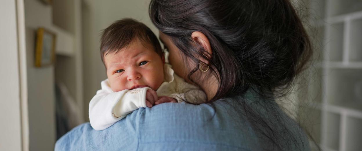 baby facing away from camera holding newborn over her shoulder who is wide awake