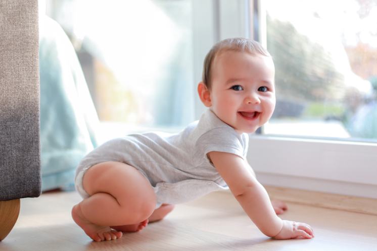Baby smiling at camera while moving into a crawling position during a longer wake window of the 3 to 2 nap transition.